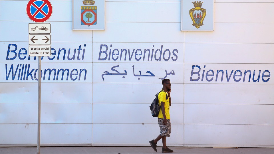A person walks in front of a wall that says "Welcome" in different languages.