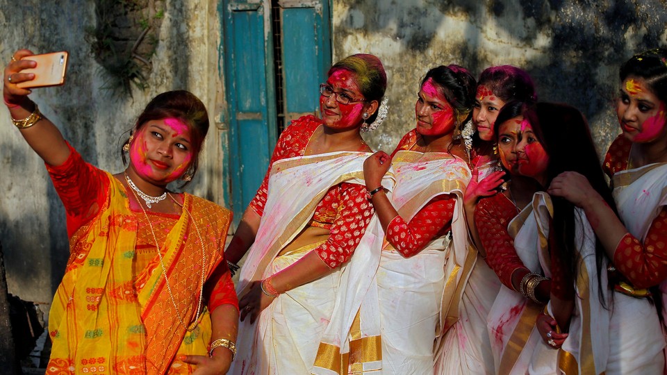 A group of women with colored powder on their faces take a selfie with a smartphone.