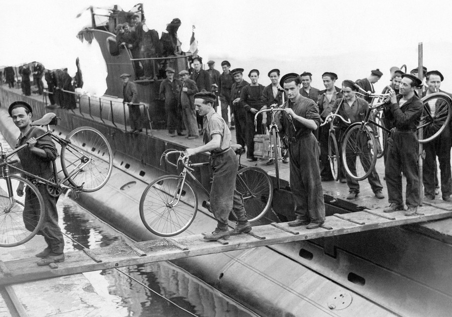 Sailors carry bicycles with them as they disembark from a submarine.