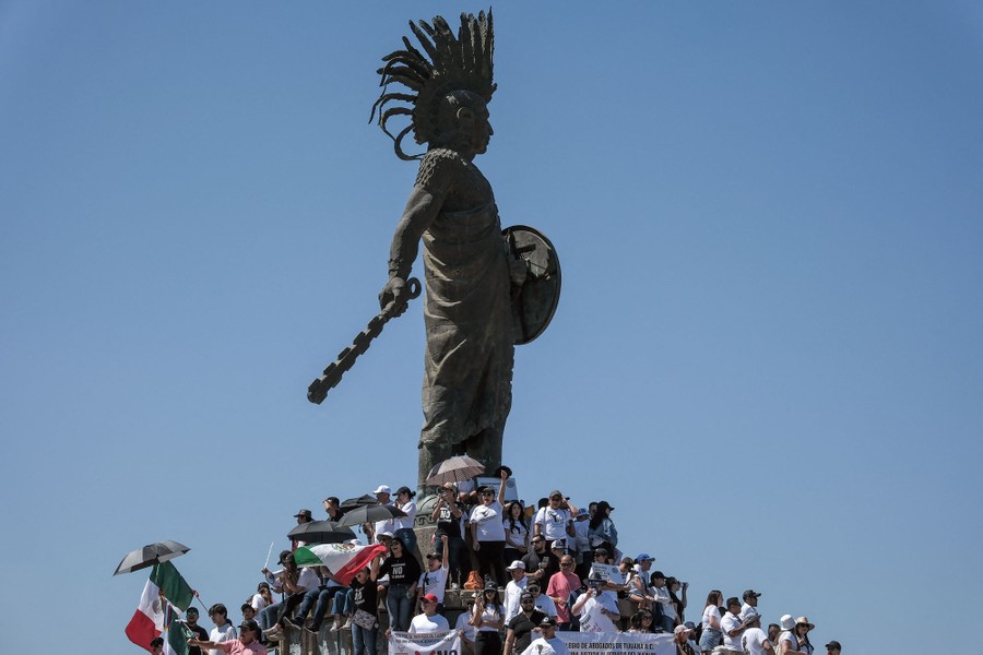 A group of protesters stand at the base of a tall statue.