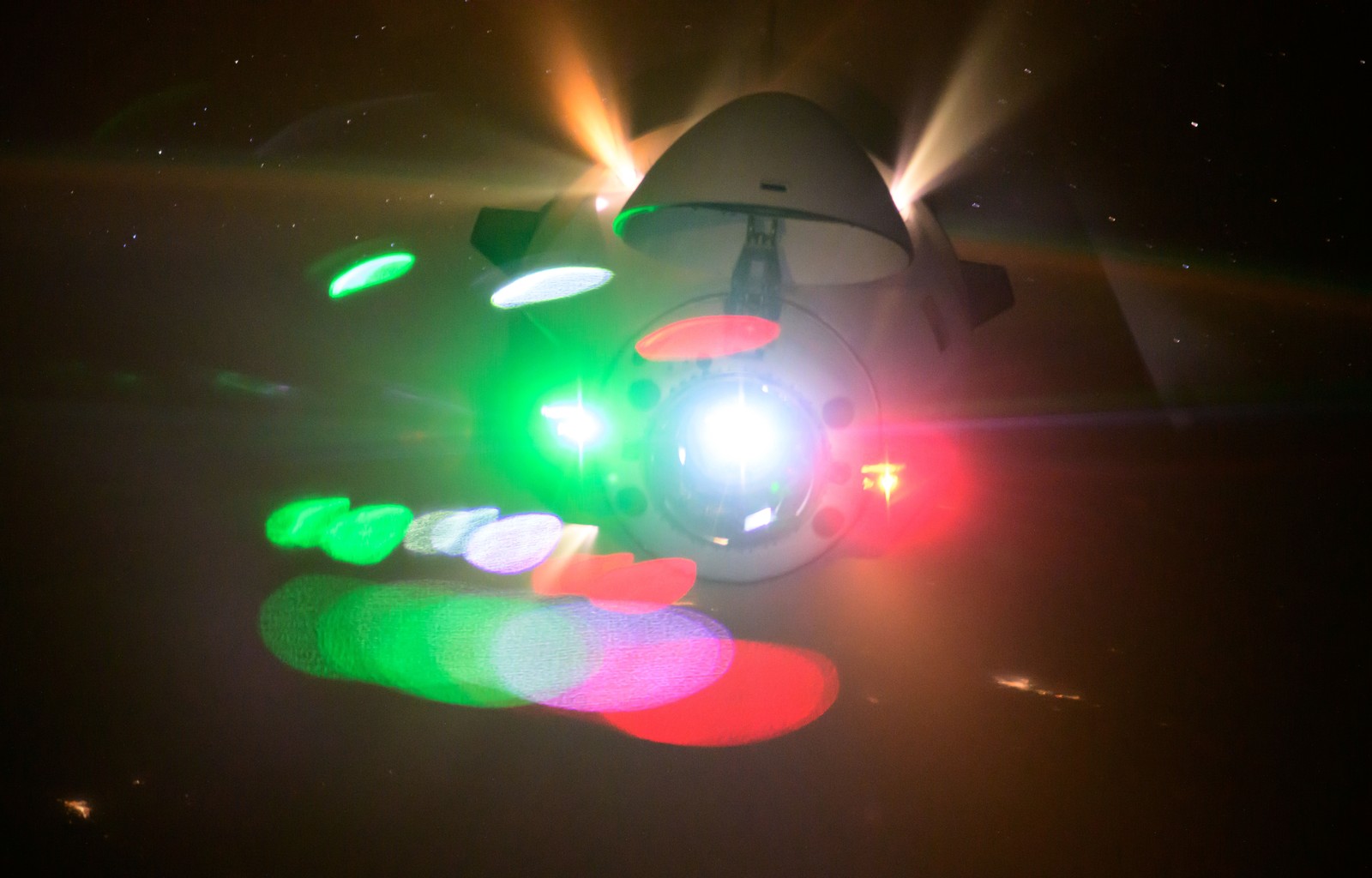 Thrusters fire and green navigation lights shine from an approaching spacecraft.