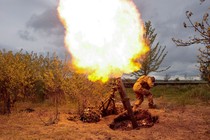 A bright flash of fire blazes above a mortar launcher as a soldier ducks nearby.