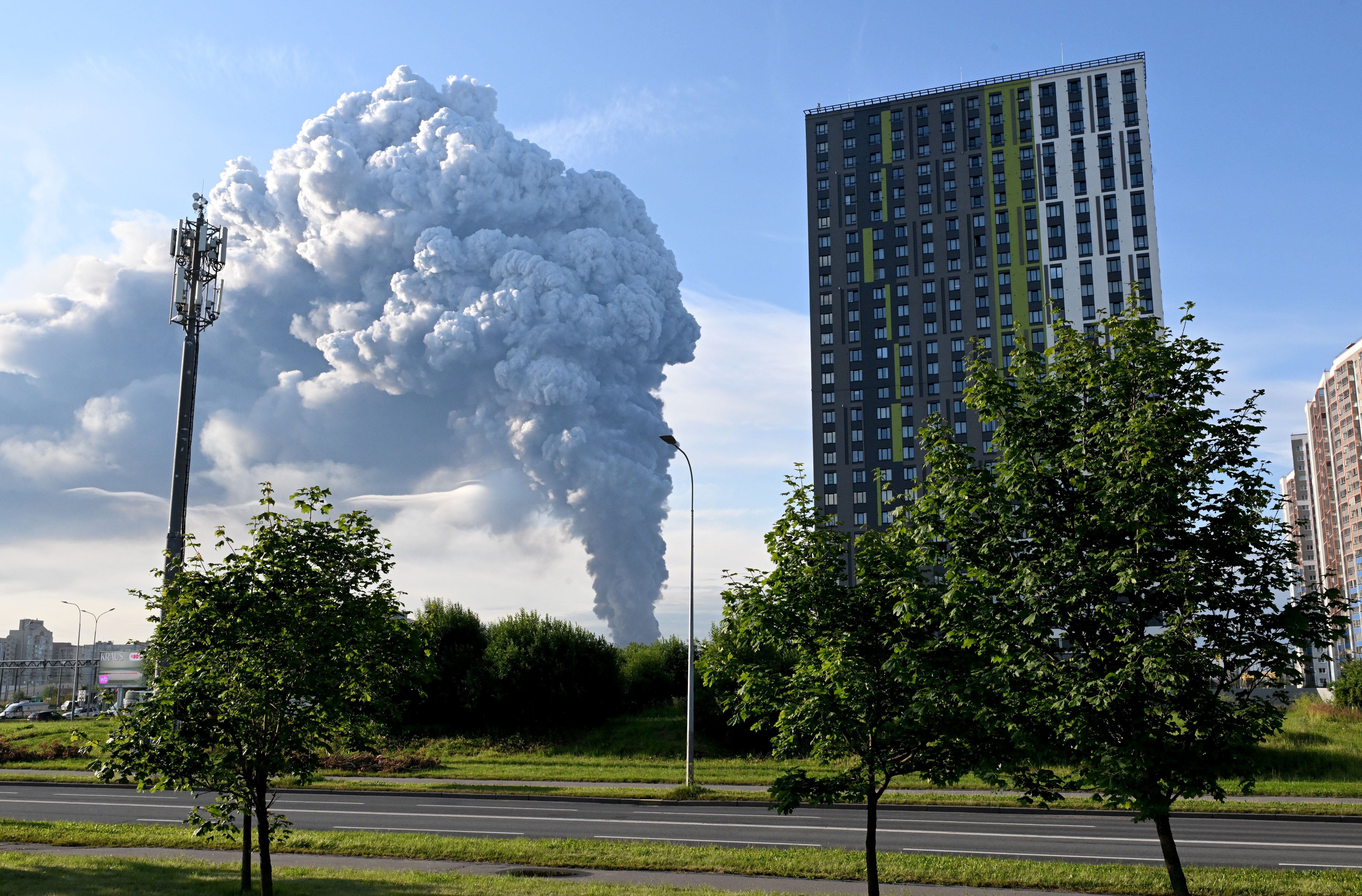 A large plume of smoke rises, seen beyond tall buildings.