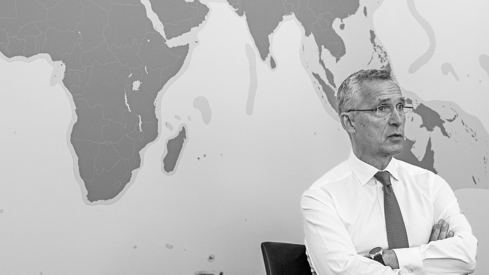 Jens Stoltenberg sits with his arms folded in front of a map of the world.