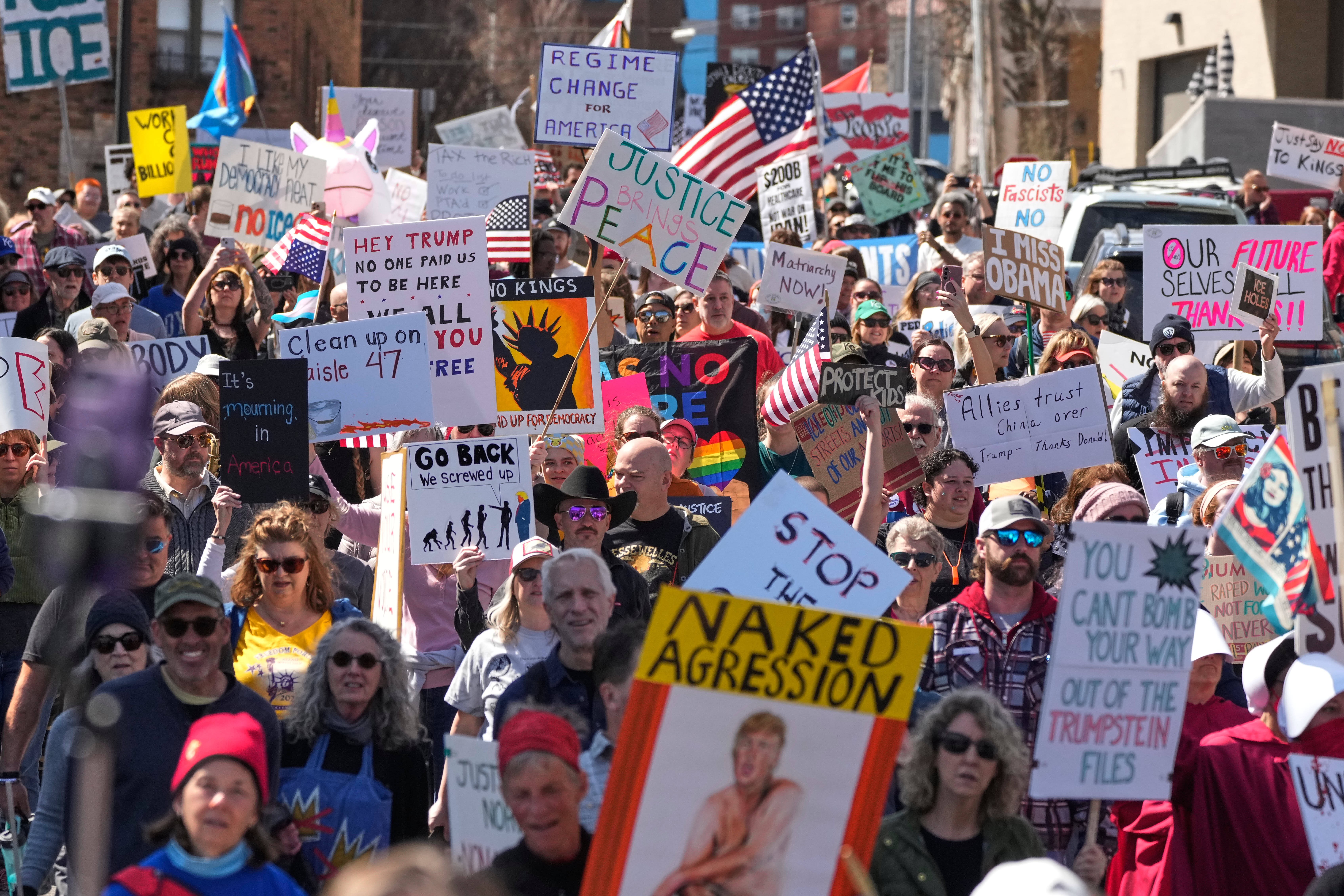 Protesters march, carrying anti-Trump signs through a shopping district.