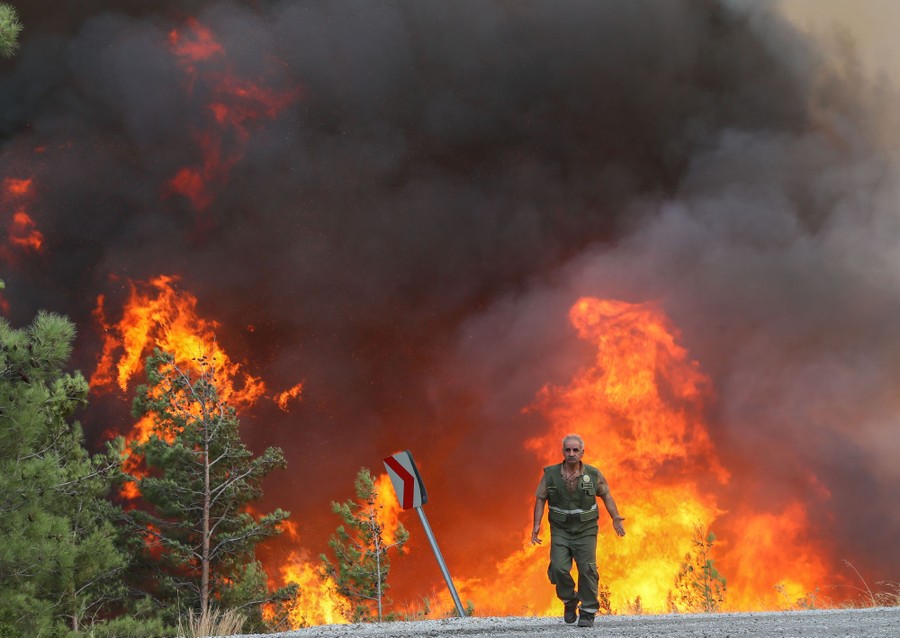 A firefighter walks in front of a large flame along a roadside.