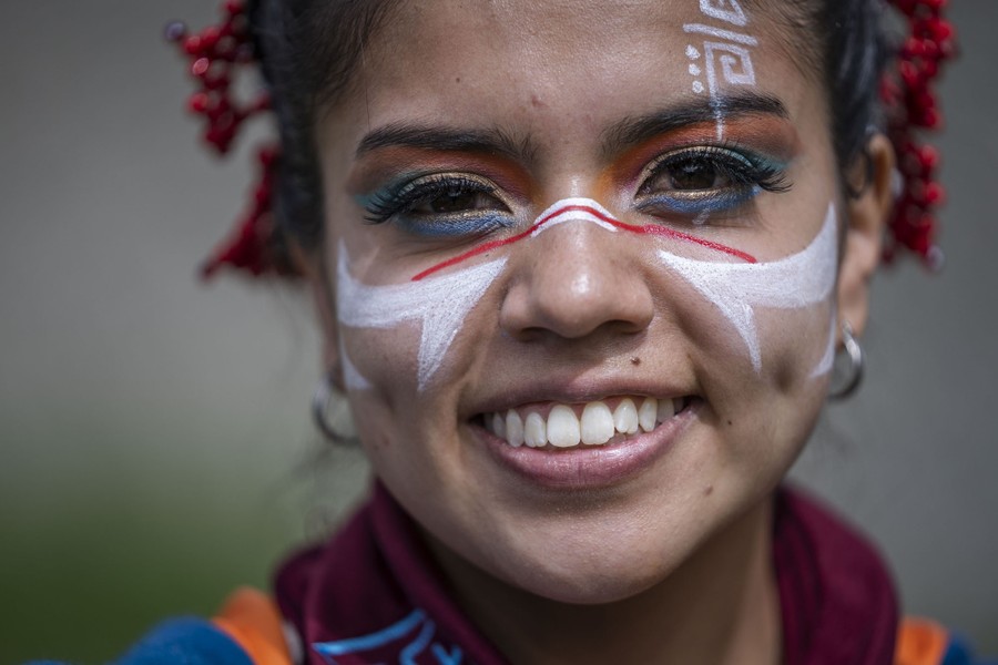 A person poses for a portrait, smiling and displaying makeup and facepaint.