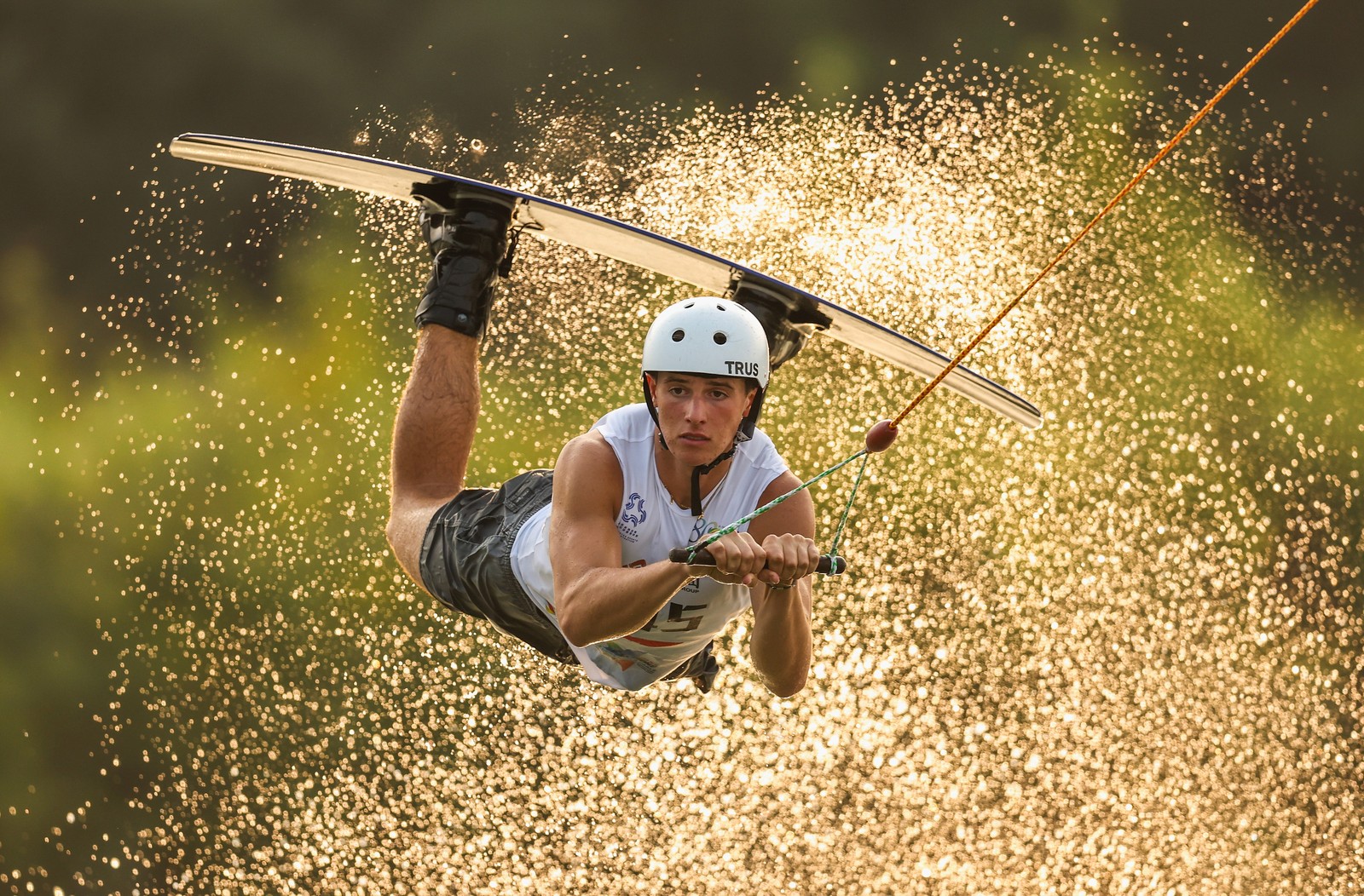A wakeboarder holds onto a tow rope as they take a jump, kicking up a spray of water.