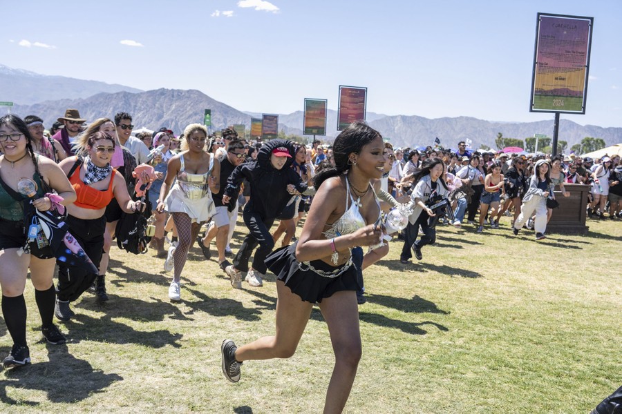 A crowd of concertgoers run across a grassy field.