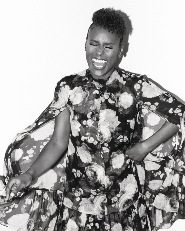 A black-and-white photo of Issa Rae laughing, wearing a floral dress in front of a white backdrop