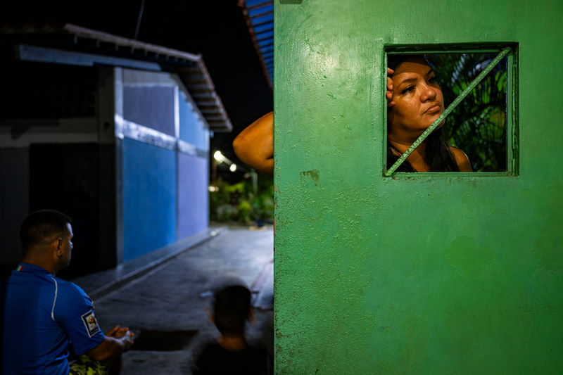 a woman gazes through an opening in a bright green door, with a blue-painted building in the background