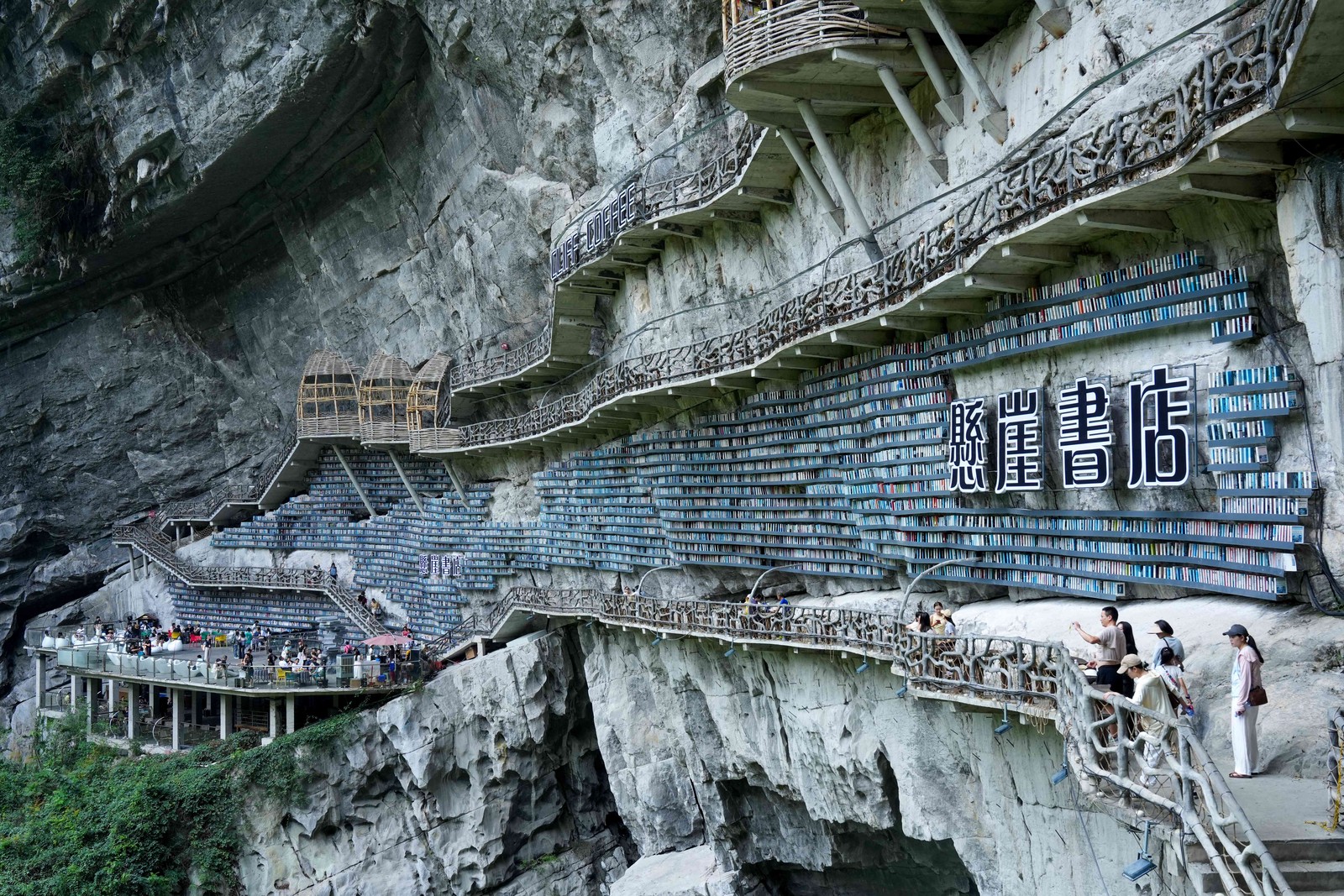 Long walkways are built onto the side of a steep rock cliff, which is lined with many rows of bookshelves.