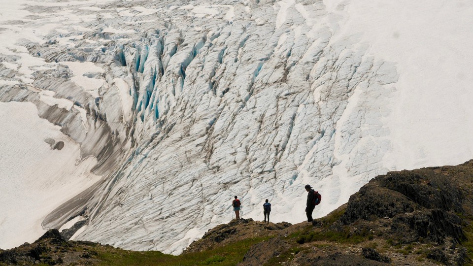 Hikers stand on a cliff overlooking Exit Glacier, in Alaska's Kenai Fjords National Park
