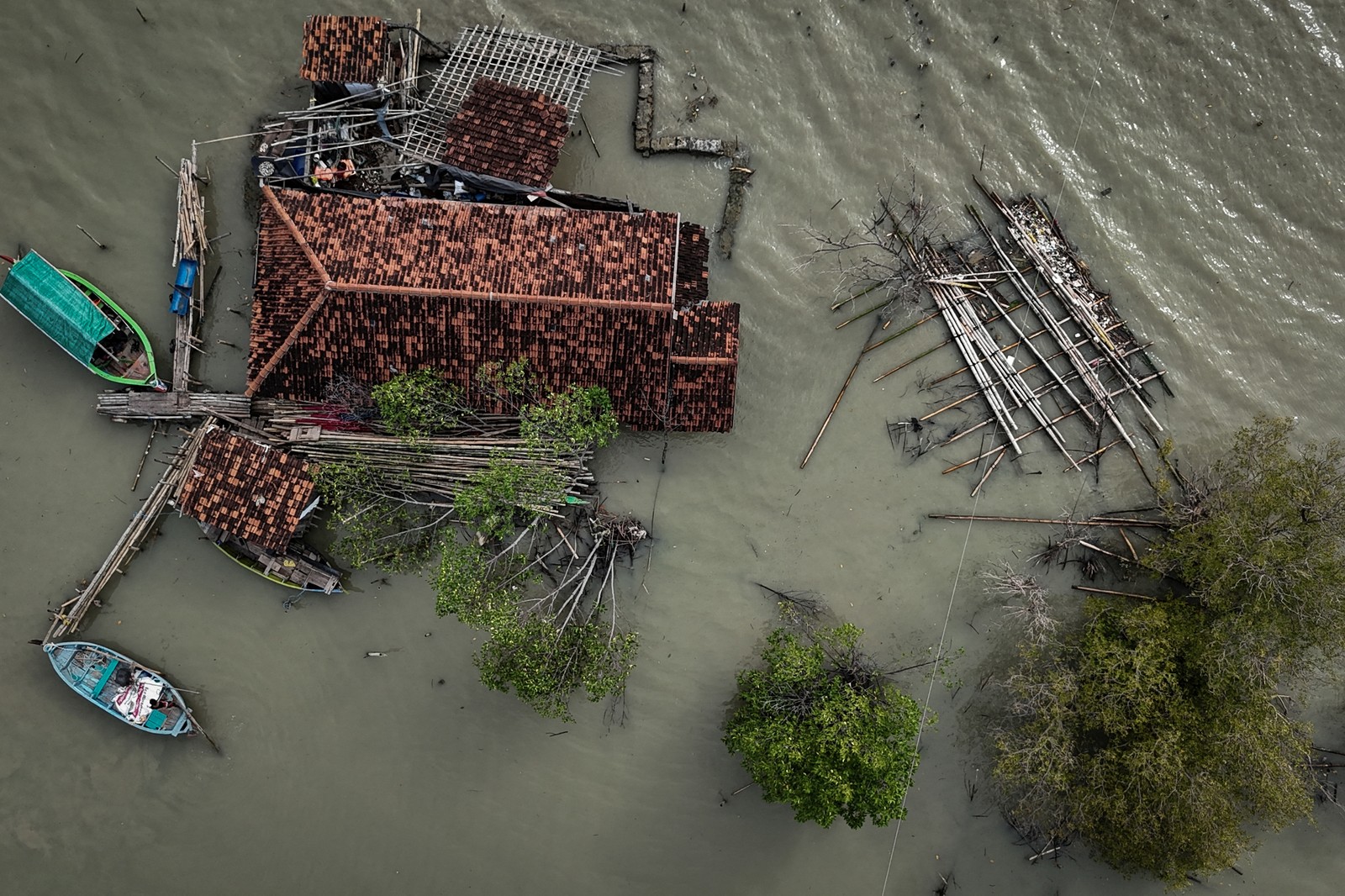 A drone view of a damaged house surrounded by seawater, debris, and trees.