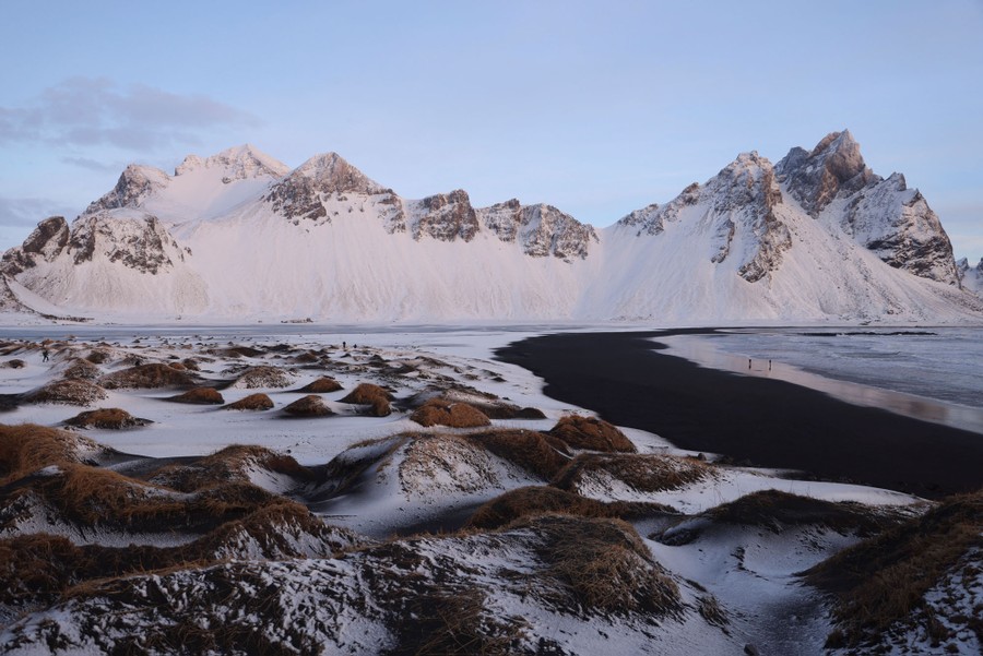A view of snow-covered mountains and a black sand beach.