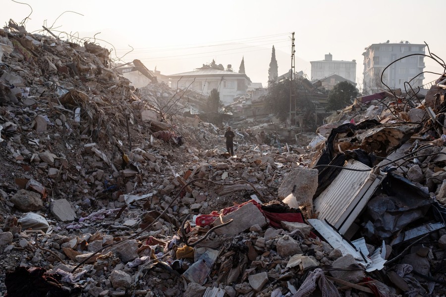 A man walks in an enormous pile of debris from a collapsed building.
