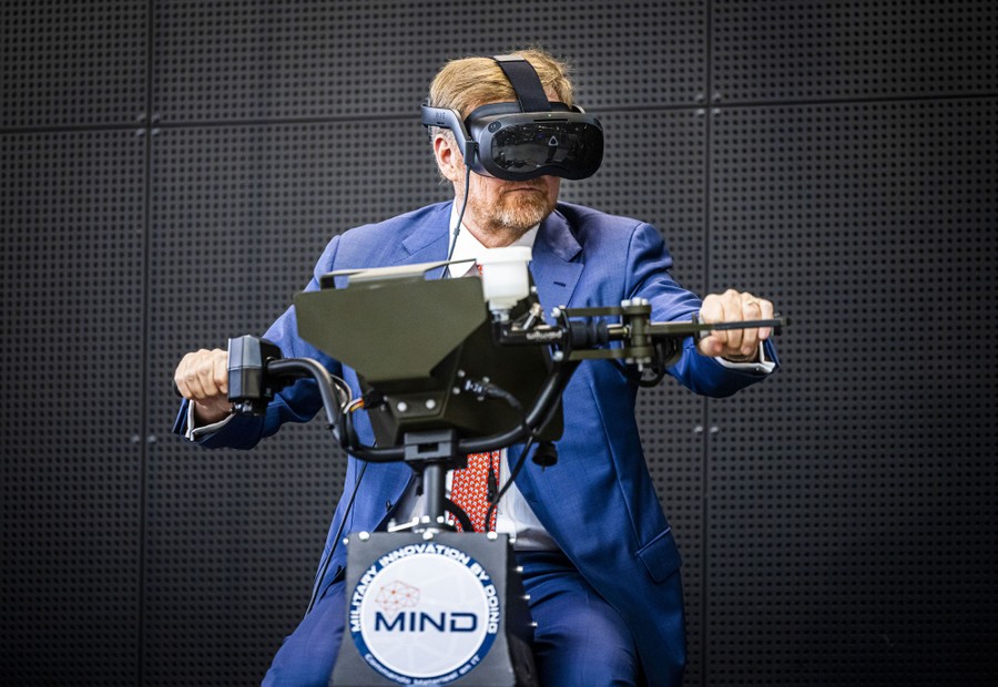 A man in a suit wears VR goggles and holds on to handlebars.