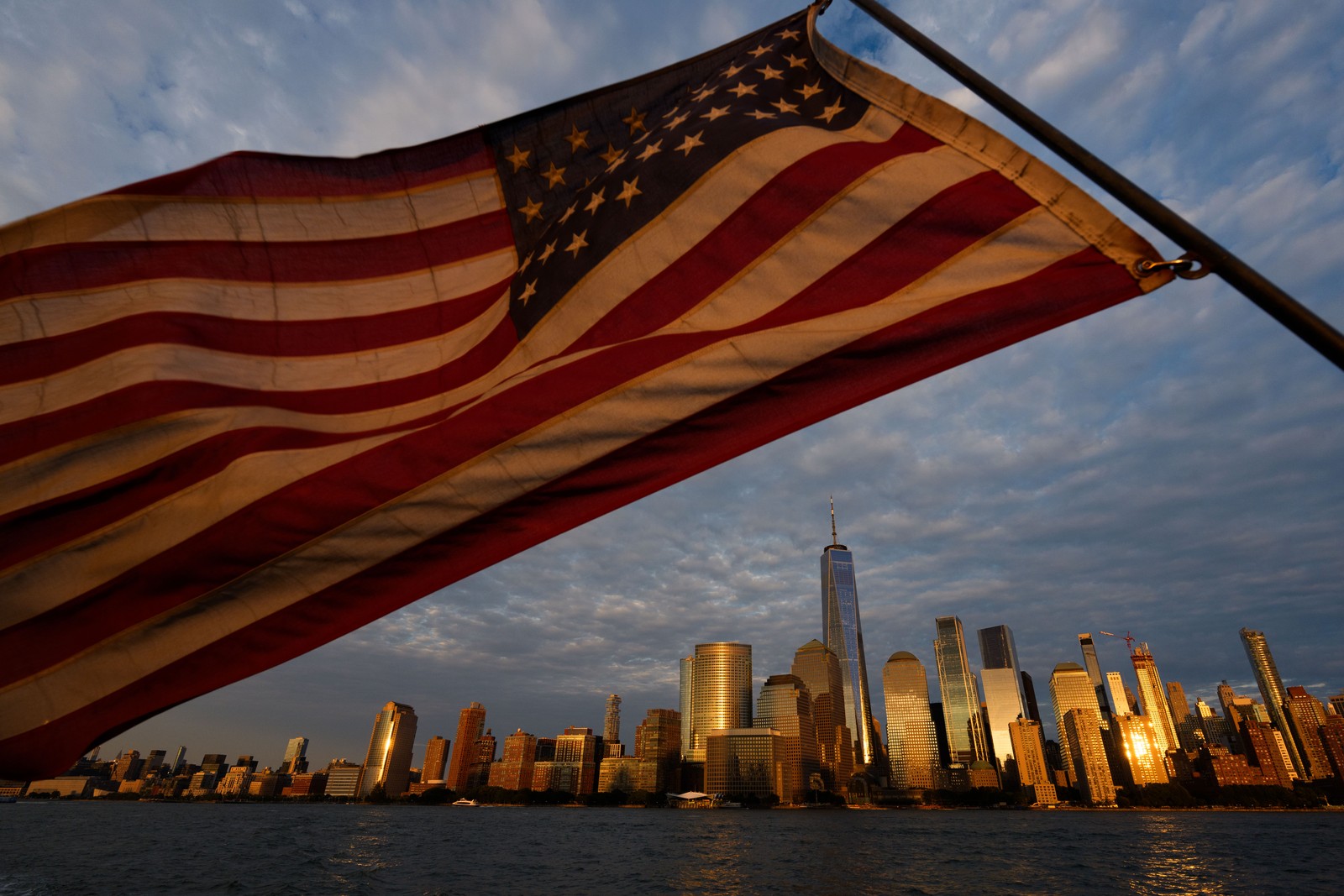 An American flag flies, with the lower Manhattan skyline in background.