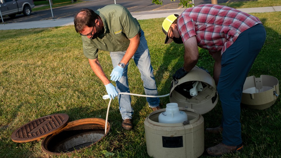 Officials collect a wastewater sample from a Montana State University sewage line.
