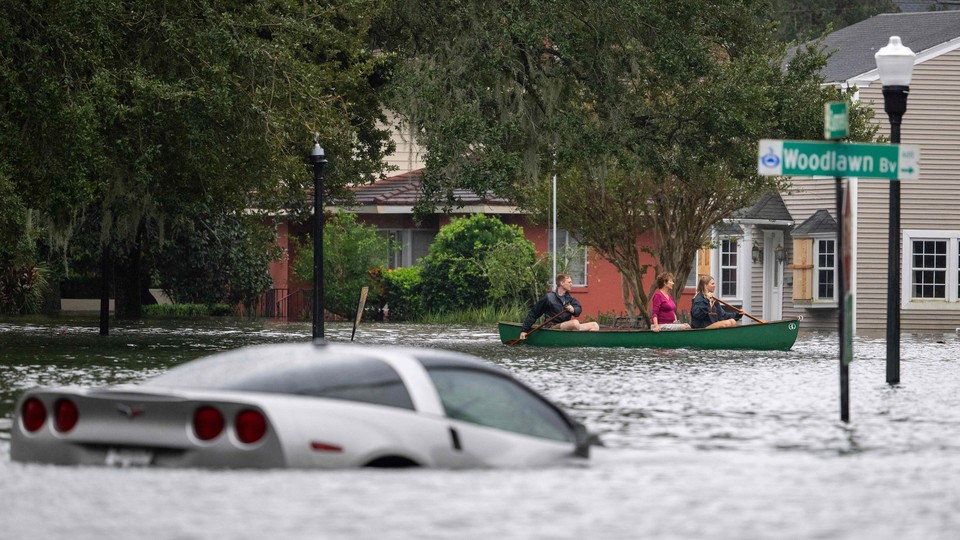 a car is submerged in water in a flooded street while people paddle past it in a canoe