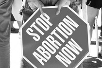 Person timidly holding sign that says "stop abortion now"