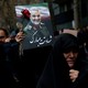 A protester in the middle of a crowd in Iran holds a rose and a photograph of Qassem Soleimani.