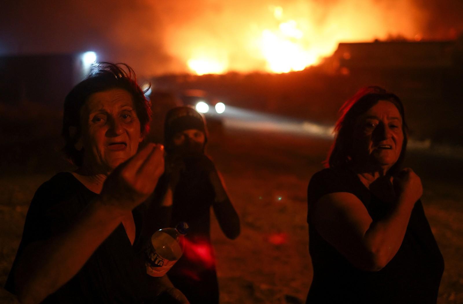 Several people gesture and speak as they walk in front of a distant wildfire.