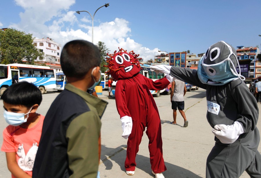 Two costumed characters mock-fight, a battle of mask versus COVID-19.