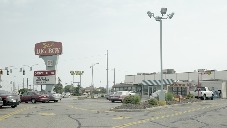 A giant parking lot outside a restaurant; a large red sign reads "Frisck's Big Boy Drive Thru: Pick up a whole coconut cream pie"