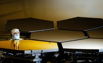 A technician, dressed in protective clothing, examines several of the James Webb Space Telescope's mirrors.