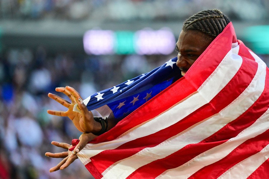 An athlete, wrapped in an American flag, reacts on a track after winning an event.