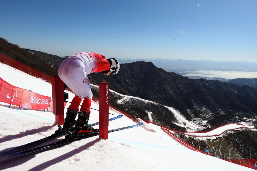 A skier stands at the top of a ski hill, preparing to start.