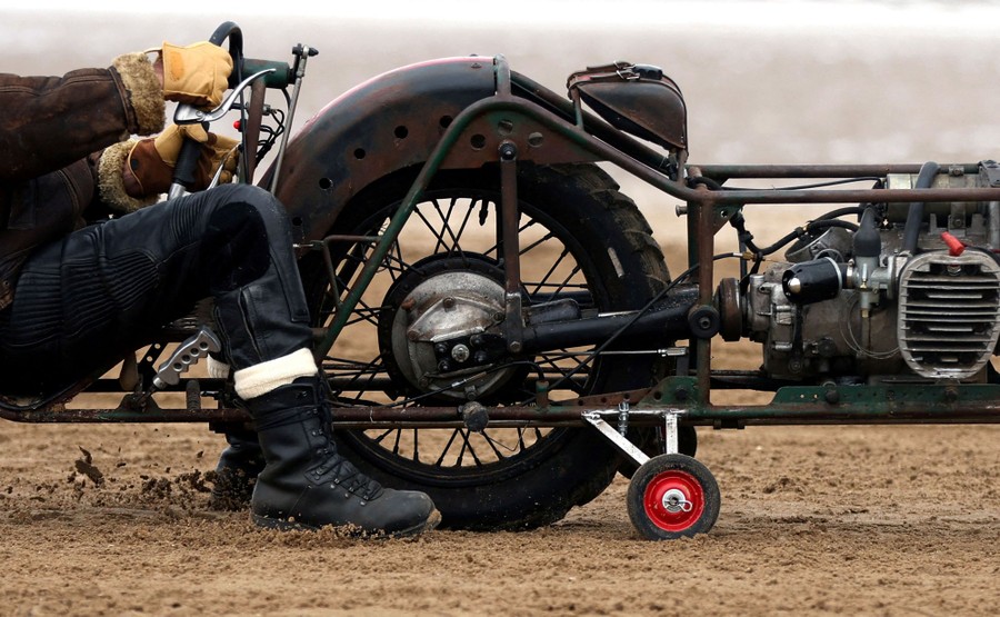 A person sits low on a wheeled vehicle on a beach.
