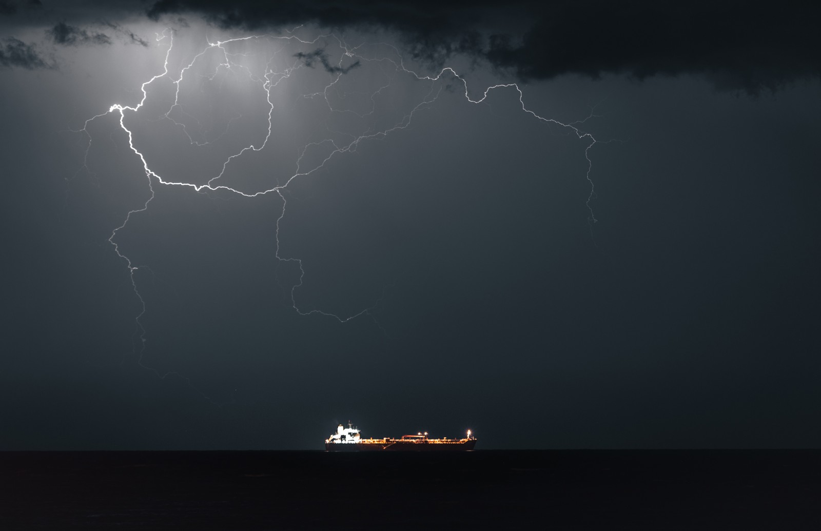 Lightning strikes in the night sky above an oil tanker.