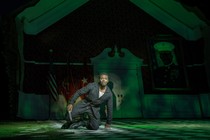 Actor in green light kneeling on ground with a knife