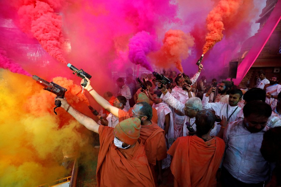 A group of people hold devices in their hands that look like pistols, shooting out clouds of colored smoke.