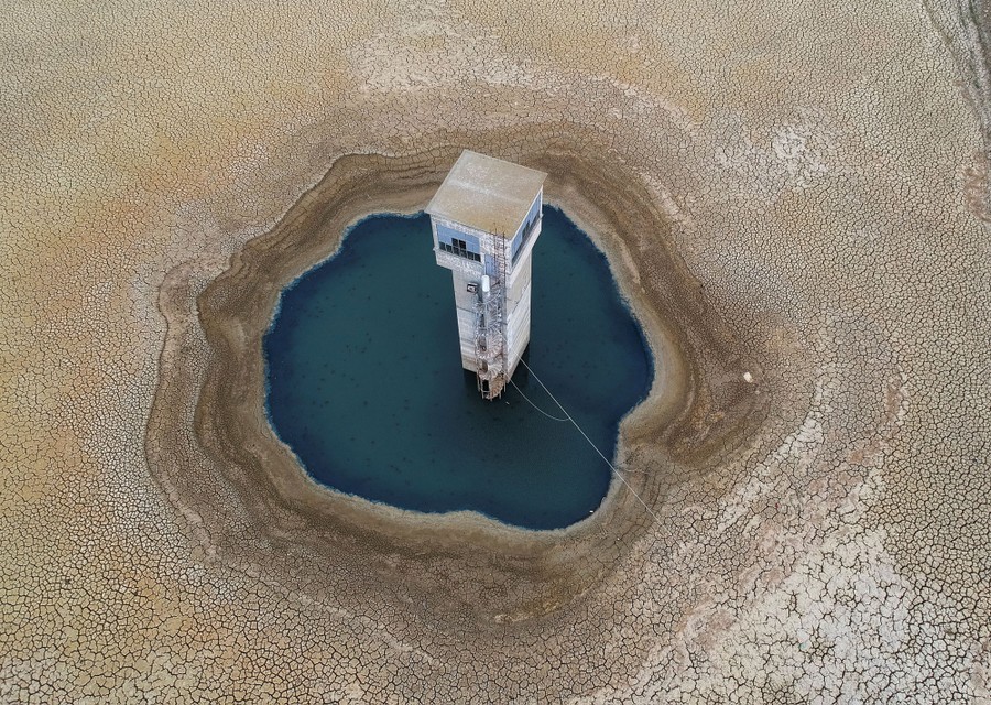 An aerial view of a narrow tower standing in a small pond in a low spot of a dry reservoir