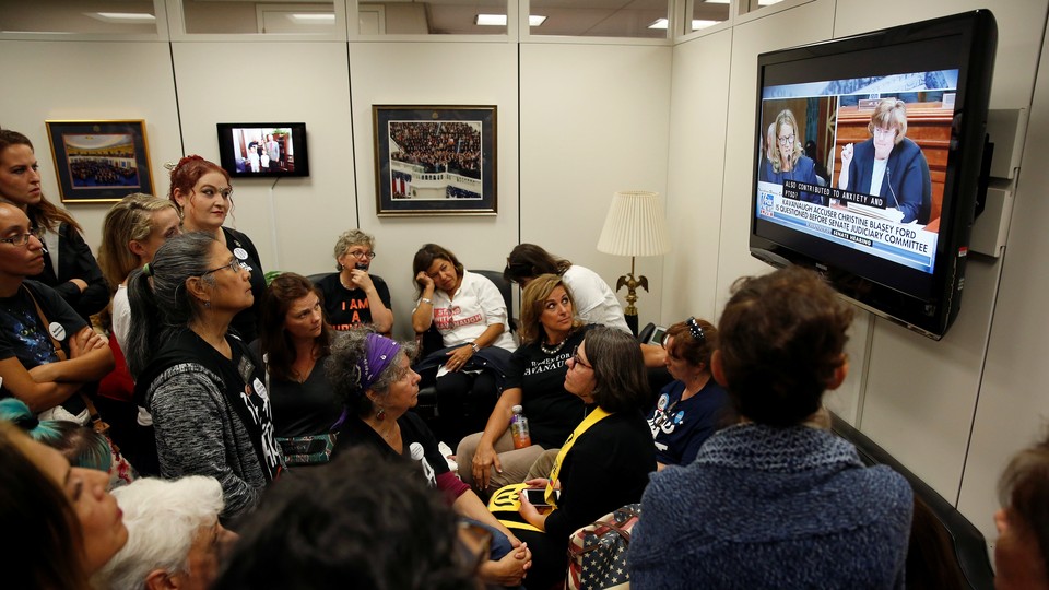 People crowd into a room to watch Christine Blasey Ford testify on TV.
