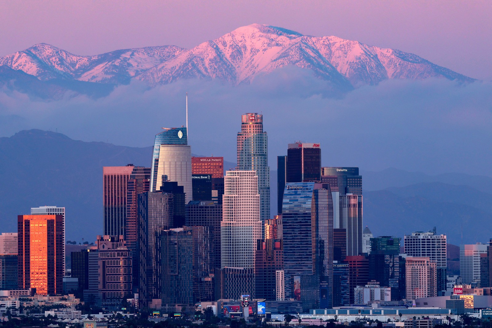 A view of the downtown Los Angeles skyline with a view of mountains in the background at sunset