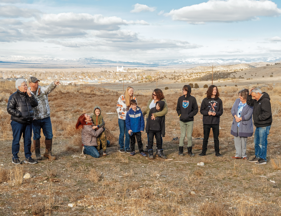 photo of group of 12 people standing in line, some hugging, on grassy field with mountains and sky in distance