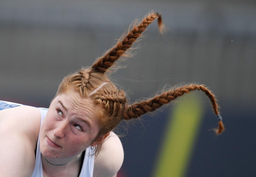 A woman throws a javelin, her braided pigtails flying in the air.