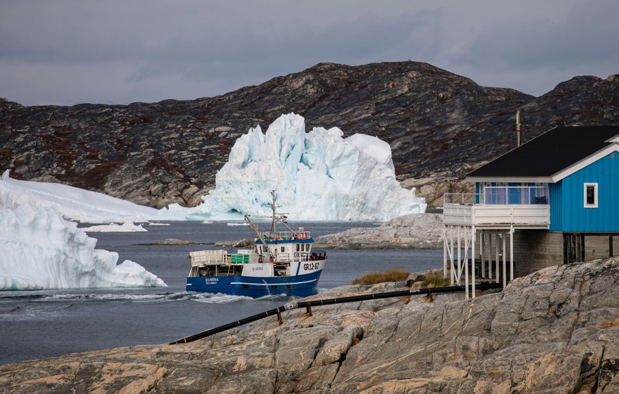 A small boat moves along the rocky shore, near several large icebergs.