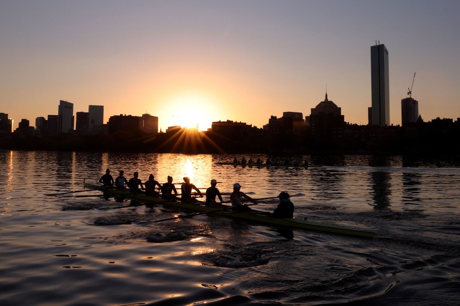 Two rowing crews on a river with Boston's city skyline in the background