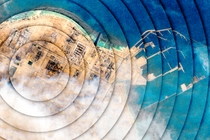 An illustration of rippling concentric circles overlayed on an overheard view of the Qatari LNG energy plant