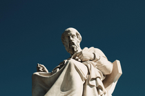 Color photograph of a marble statue of Plato seen in front of a dark-blue background.