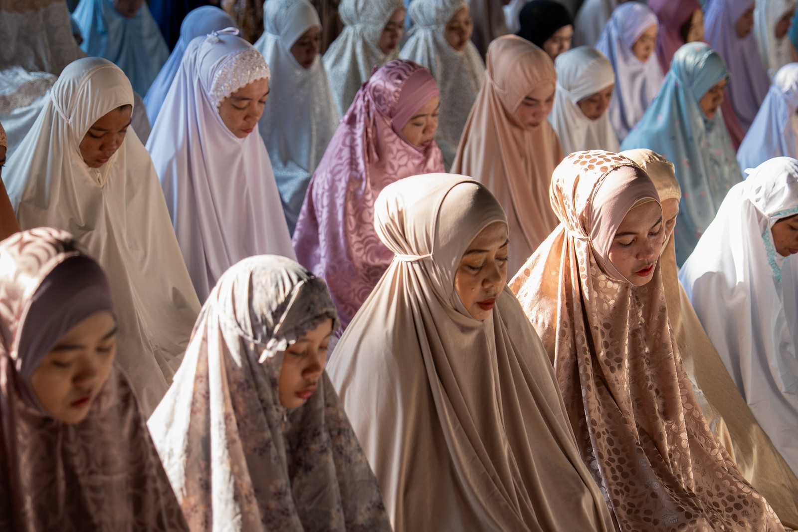 Women wearing different colored hijabs sit together during prayer.