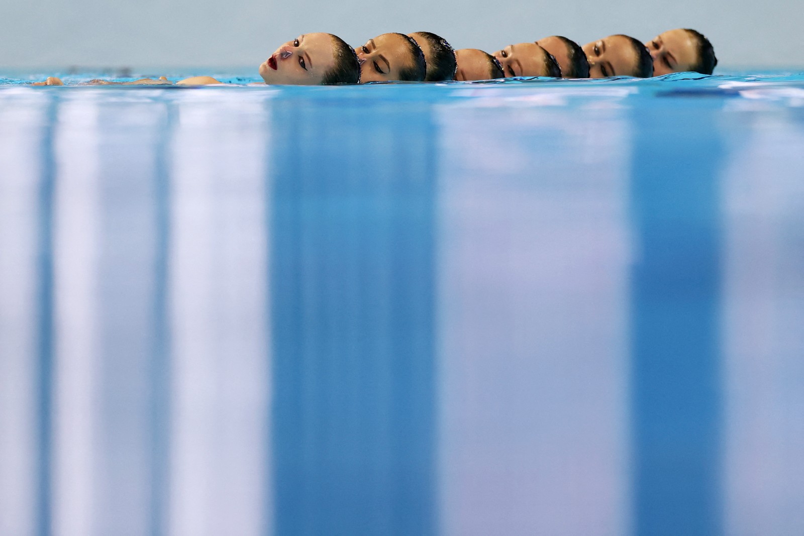 The heads of about eight synchronized swimmers, seen just above the surface of a swimming pool during a performance.