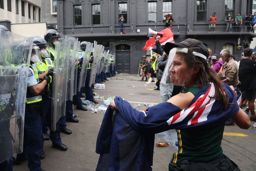 Protesters confront a line of riot police holding shields in a street.
