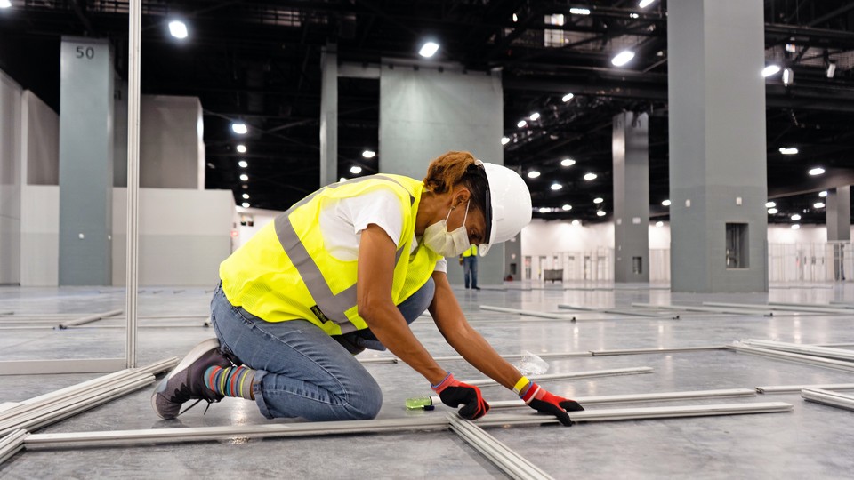 A construction worker kneels on the floor of a large room.