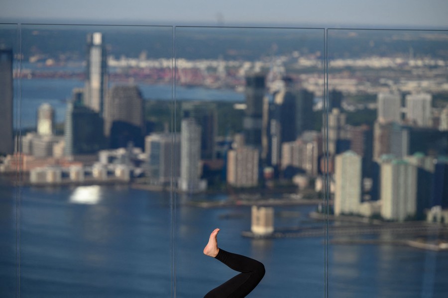 The leg of a yoga practitioner is seen, with tall buildings and water in the distant background.